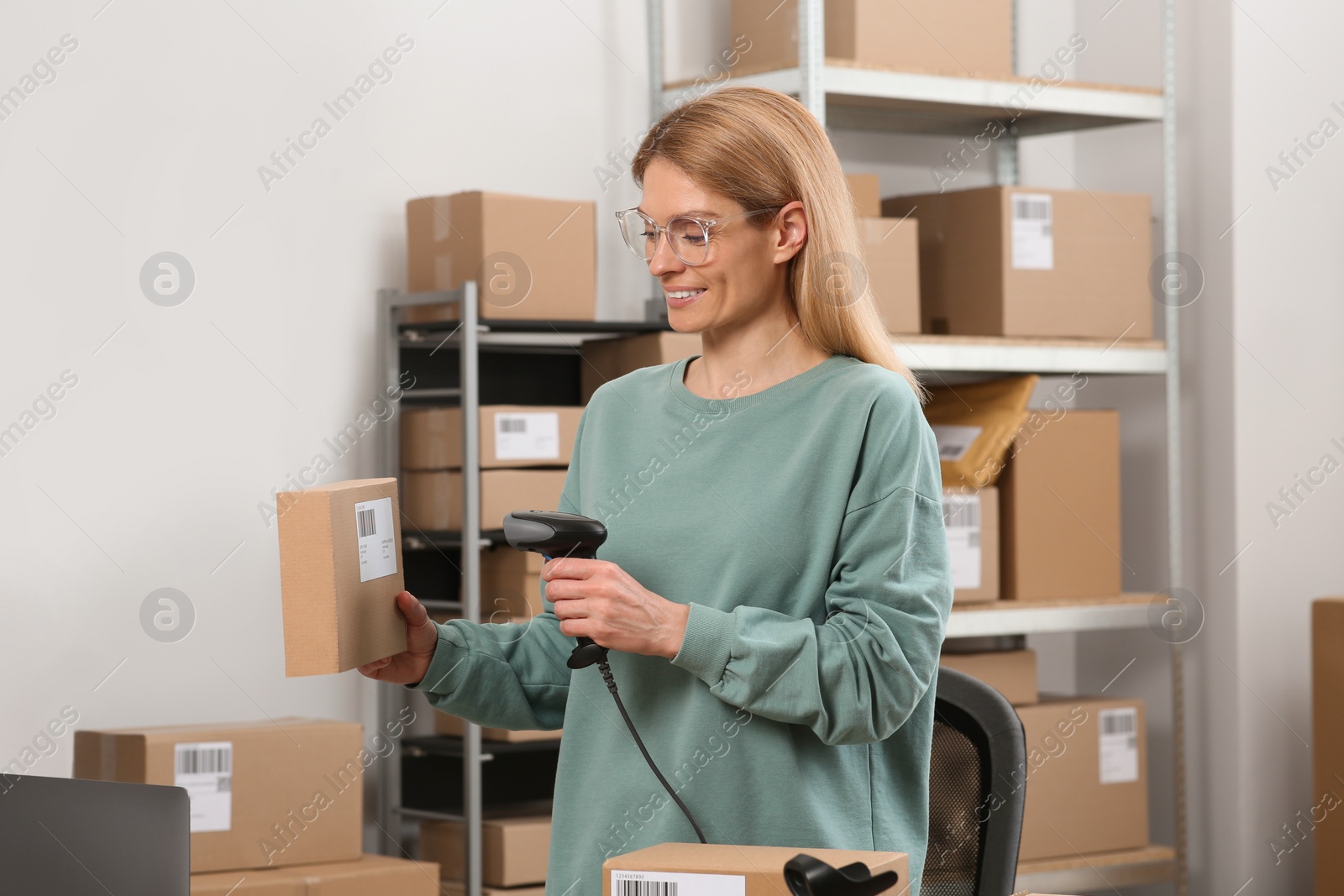 Photo of Seller with scanner reading parcel barcode in office. Online store