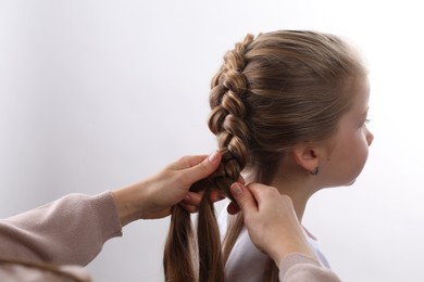 Professional stylist braiding girl's hair on white background, closeup