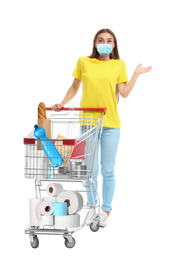 Image of Young woman in medical mask and shopping cart with purchases on white background. Coronavirus pandemic 