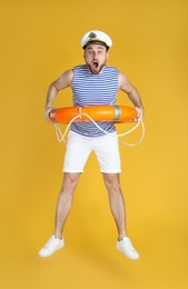 Emotional sailor with ring buoy jumping on yellow background