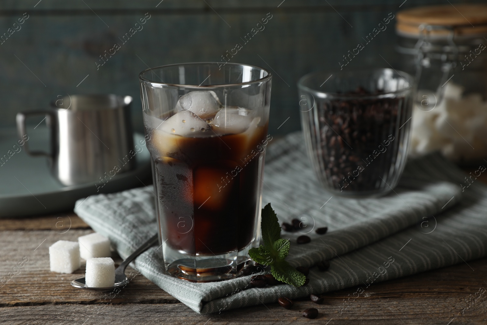 Photo of Glass of delicious iced coffee, mint and sugar cubes on wooden table