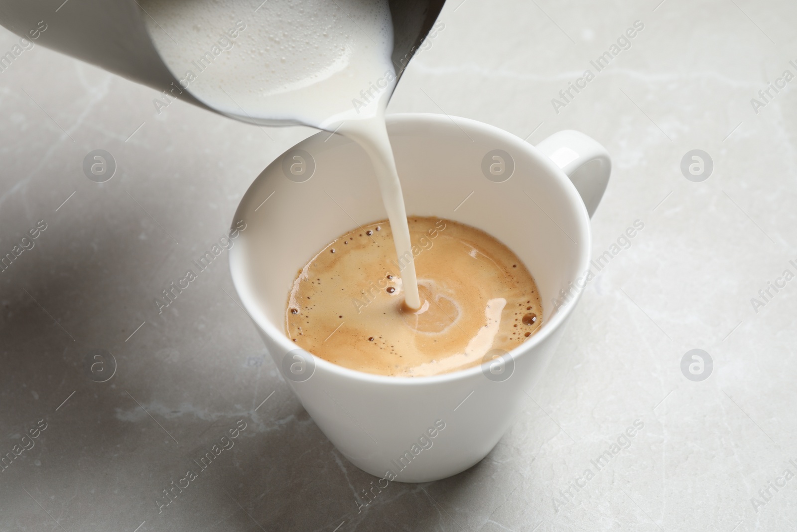 Photo of Pouring milk into cup of coffee on grey table, closeup