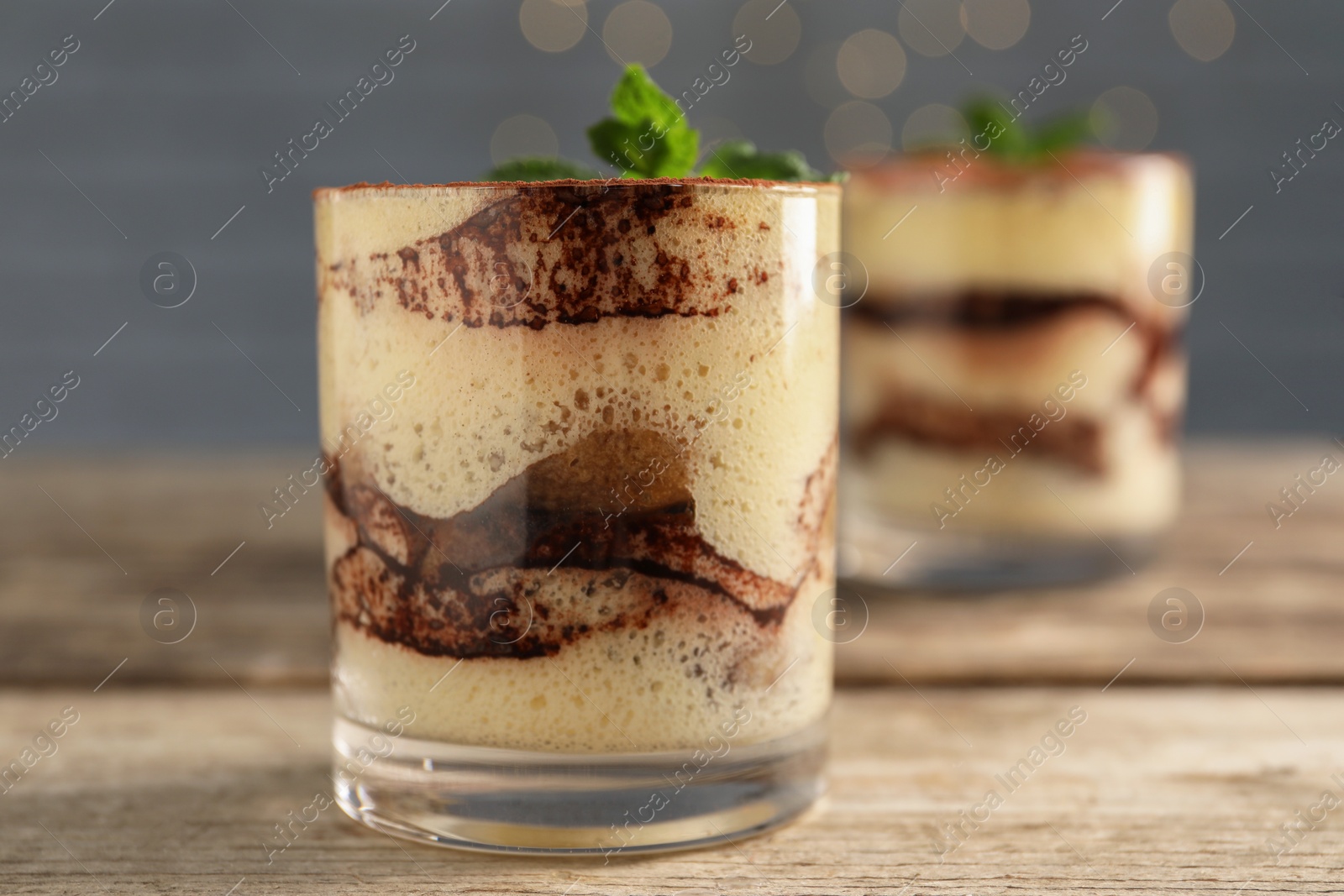 Photo of Tasty tiramisu and mint in glasses on wooden table, closeup