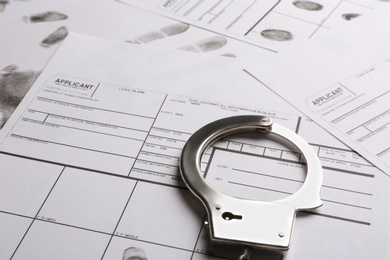 Handcuffs and fingerprint record sheets, closeup. Criminal investigation