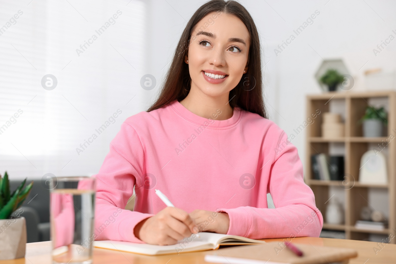 Photo of Young woman writing in notebook at wooden table indoors