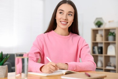 Photo of Young woman writing in notebook at wooden table indoors