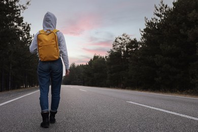 Photo of Woman with backpack going along road near forest, back view