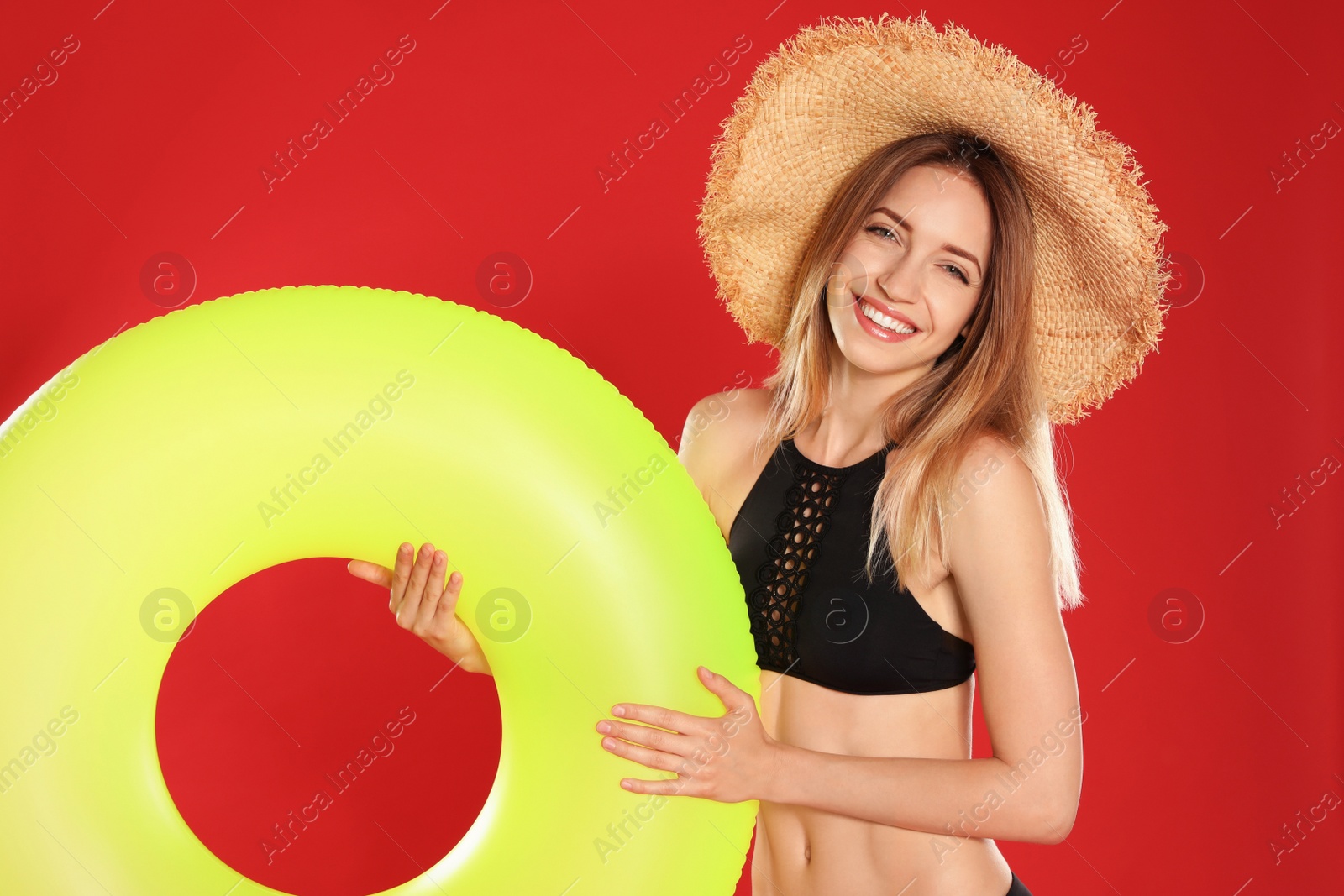 Photo of Beautiful young woman in stylish bikini with yellow inflatable ring on red background