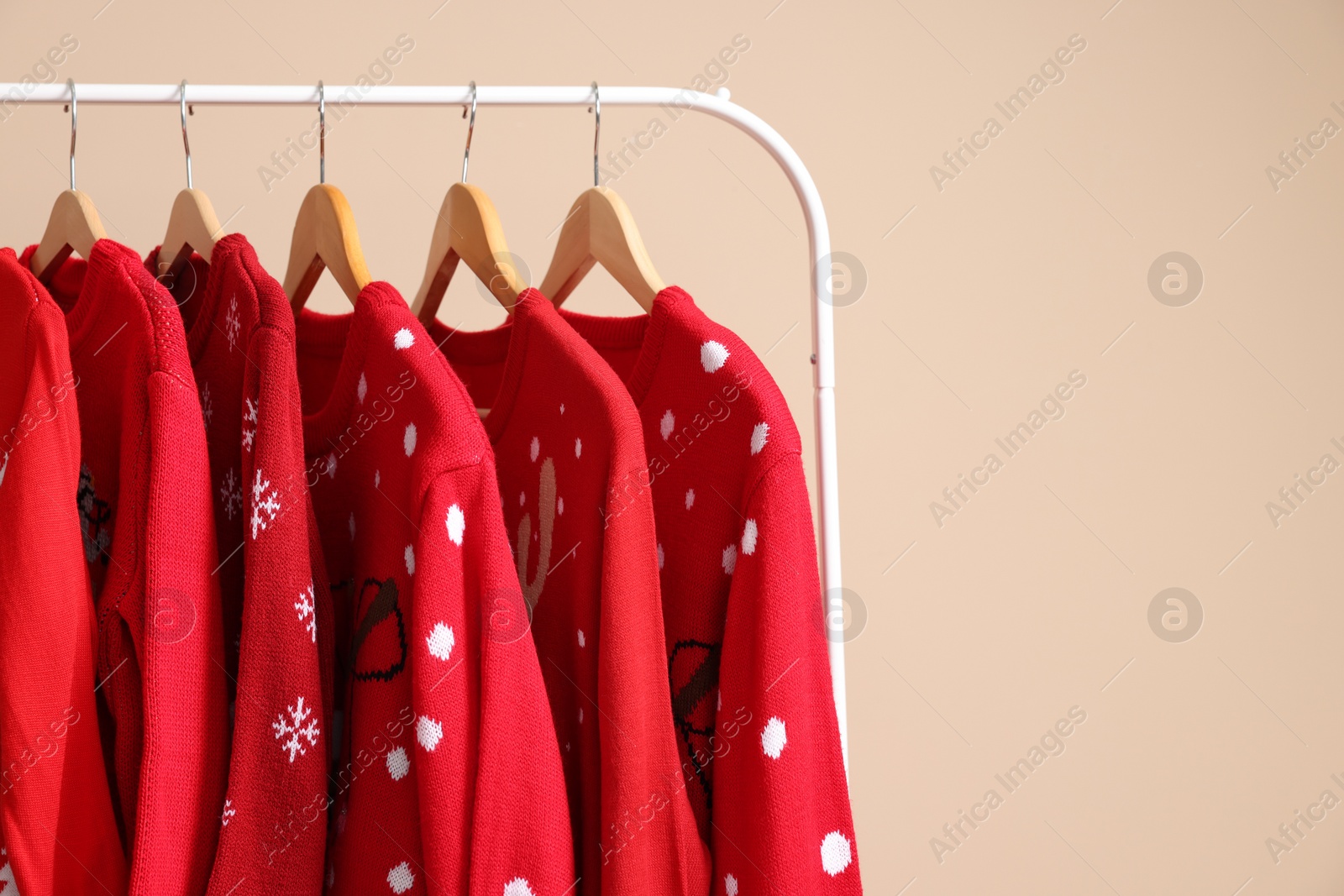 Photo of Rack with different Christmas sweaters on beige background, space for text