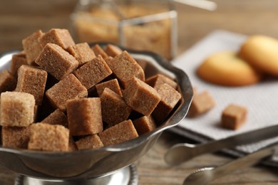 Photo of Brown sugar cubes in metal bowl on wooden table, closeup