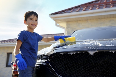 Photo of Happy little boy washing car at backyard on sunny day
