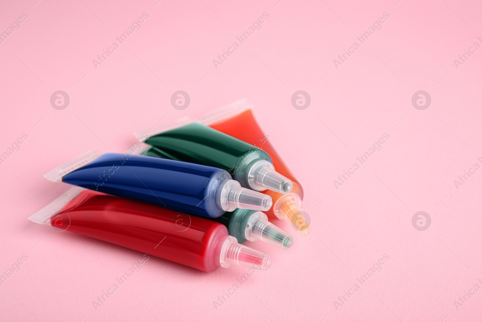 Photo of Tubes with different food coloring on pink background, space for text