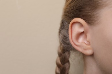 Photo of Cute little girl on beige background, closeup of ear. Space for text