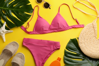 Photo of Beautiful pink bikini and beach accessories on yellow background, flat lay