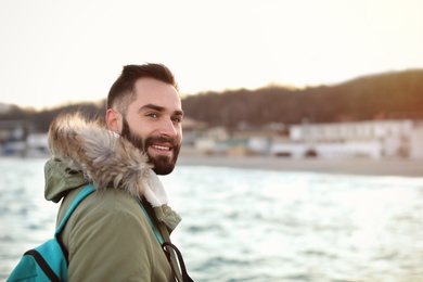 Stylish young man with backpack near sea