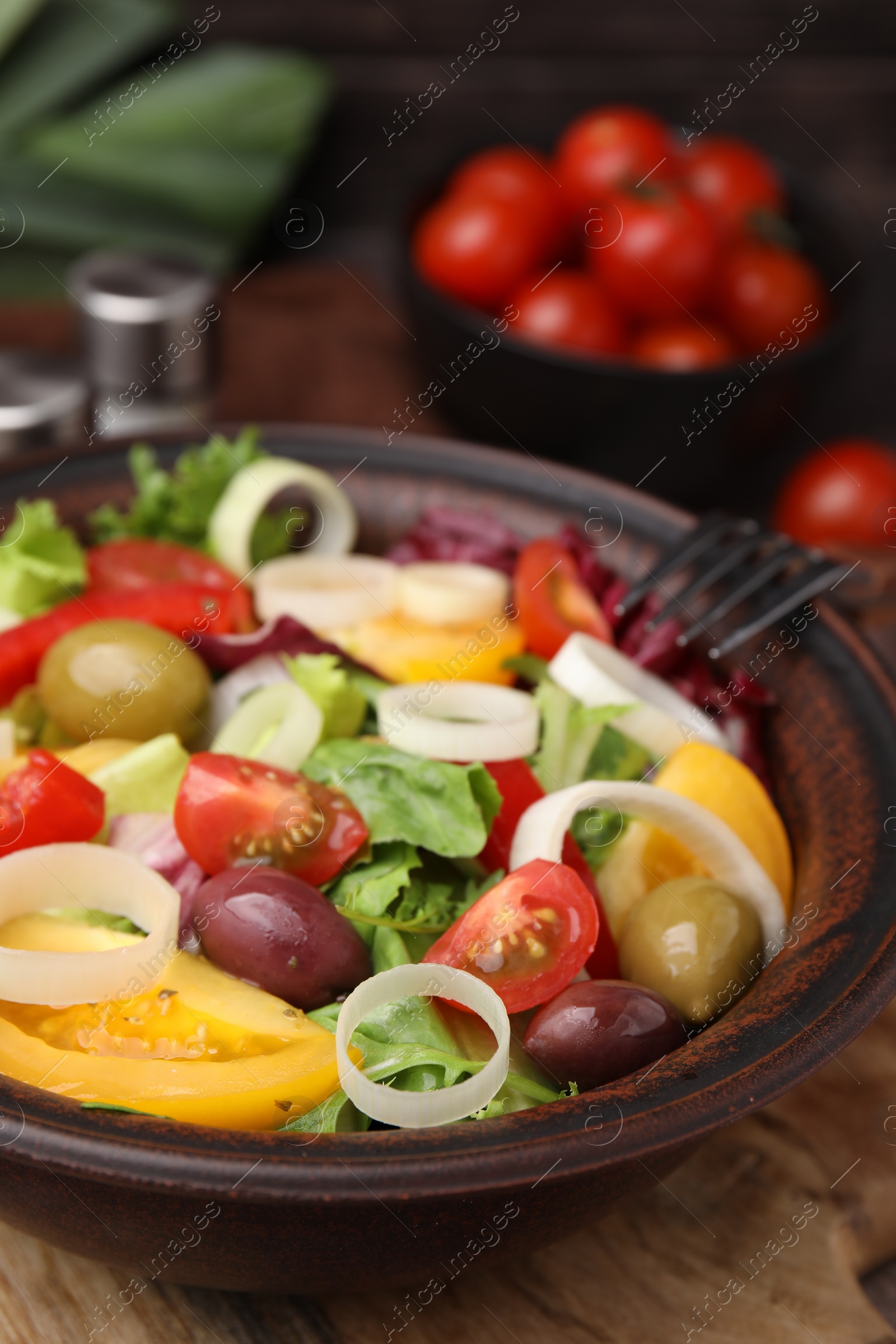 Photo of Bowl of tasty salad with leek and olives on wooden board, closeup