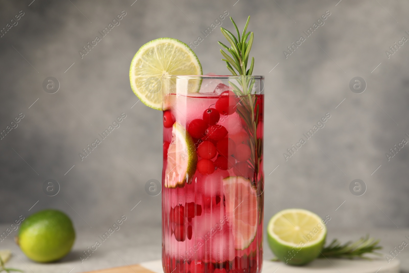 Photo of Tasty cranberry cocktail with rosemary and lime in glass on gray background, closeup