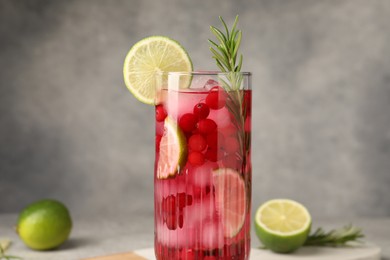 Tasty cranberry cocktail with rosemary and lime in glass on gray background, closeup