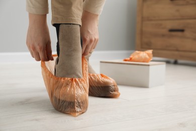 Photo of Woman wearing bright shoe covers onto her boots indoors, closeup