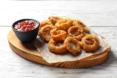 Photo of Homemade crunchy fried onion rings with tomato sauce on wooden table