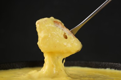 Photo of Dipping piece of bread into fondue pot with tasty melted cheese against dark gray background, closeup