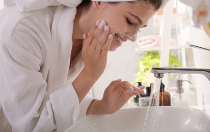 Photo of Beautiful teenage girl washing face with cleansing foam in bathroom. Skin care cosmetic