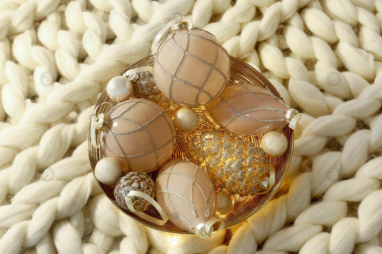 Photo of Christmas baubles in bowl on white knitted blanket, top view