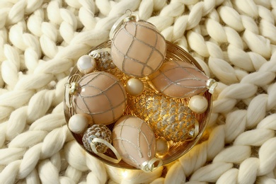 Photo of Christmas baubles in bowl on white knitted blanket, top view