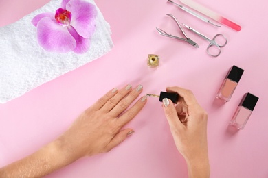 Woman applying nail polish on color background, top view