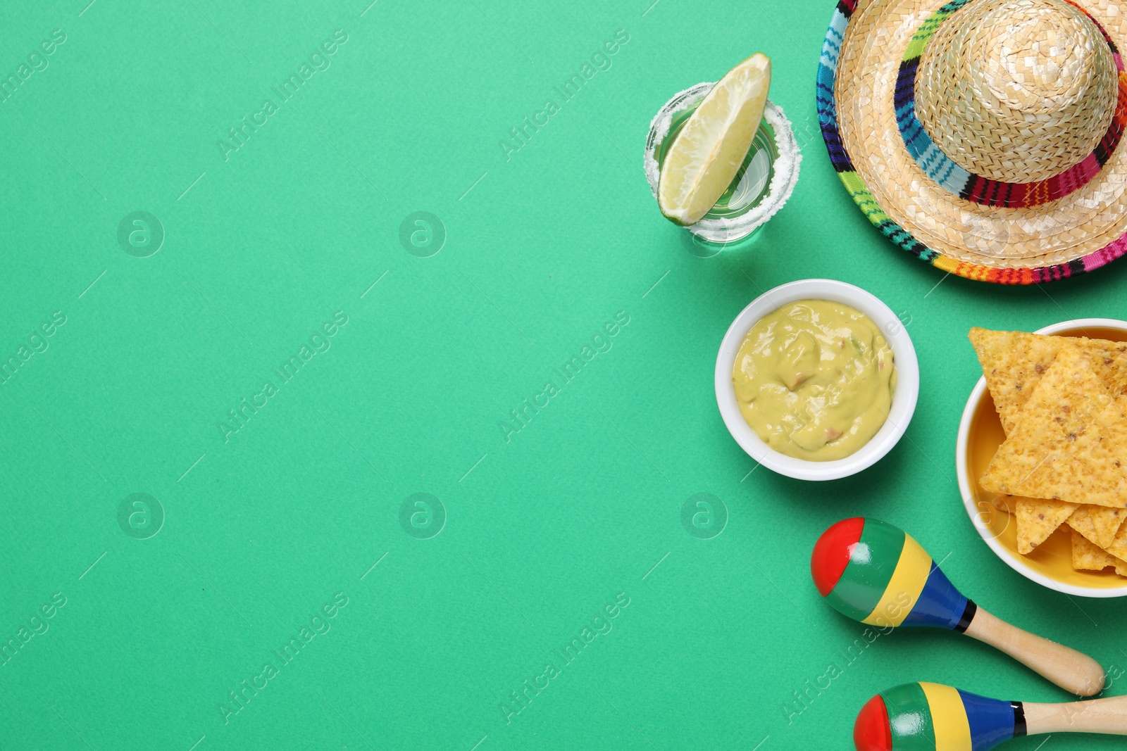 Photo of Mexican sombrero hat, guacamole, nachos chips, maracas and tequila on green background, flat lay. Space for text