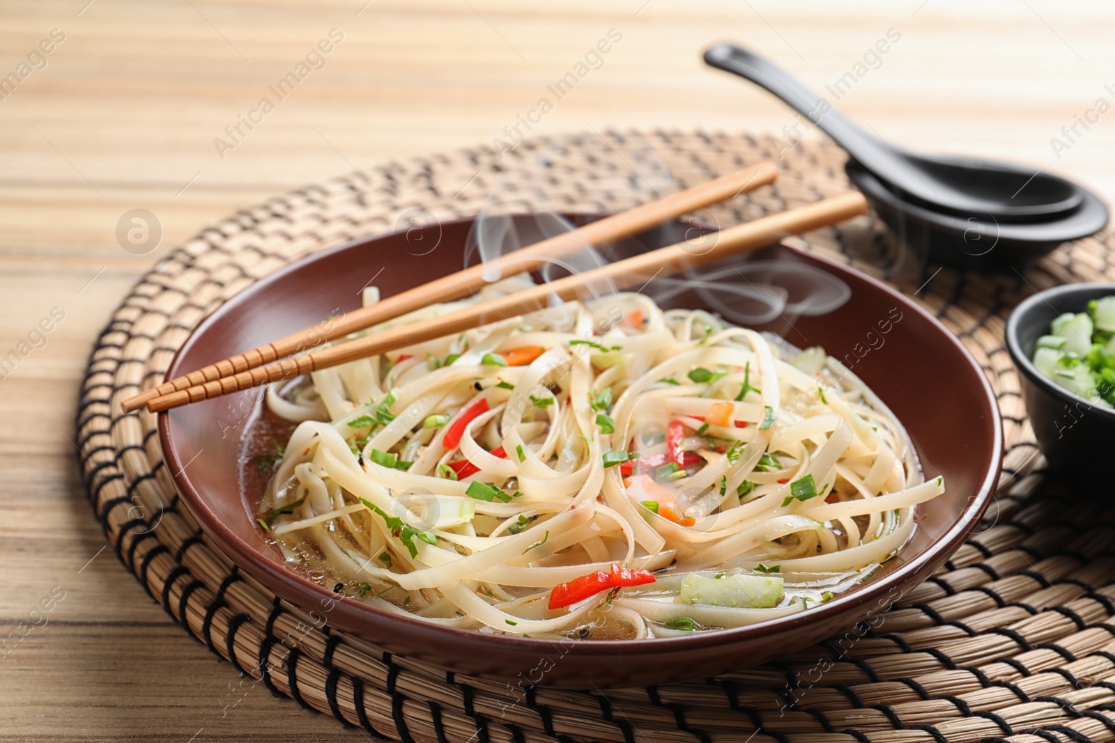 Photo of Plate of hot noodles with broth, vegetables and chopsticks on table