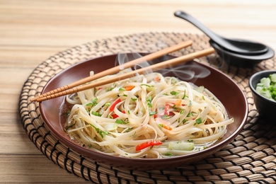 Plate of hot noodles with broth, vegetables and chopsticks on table