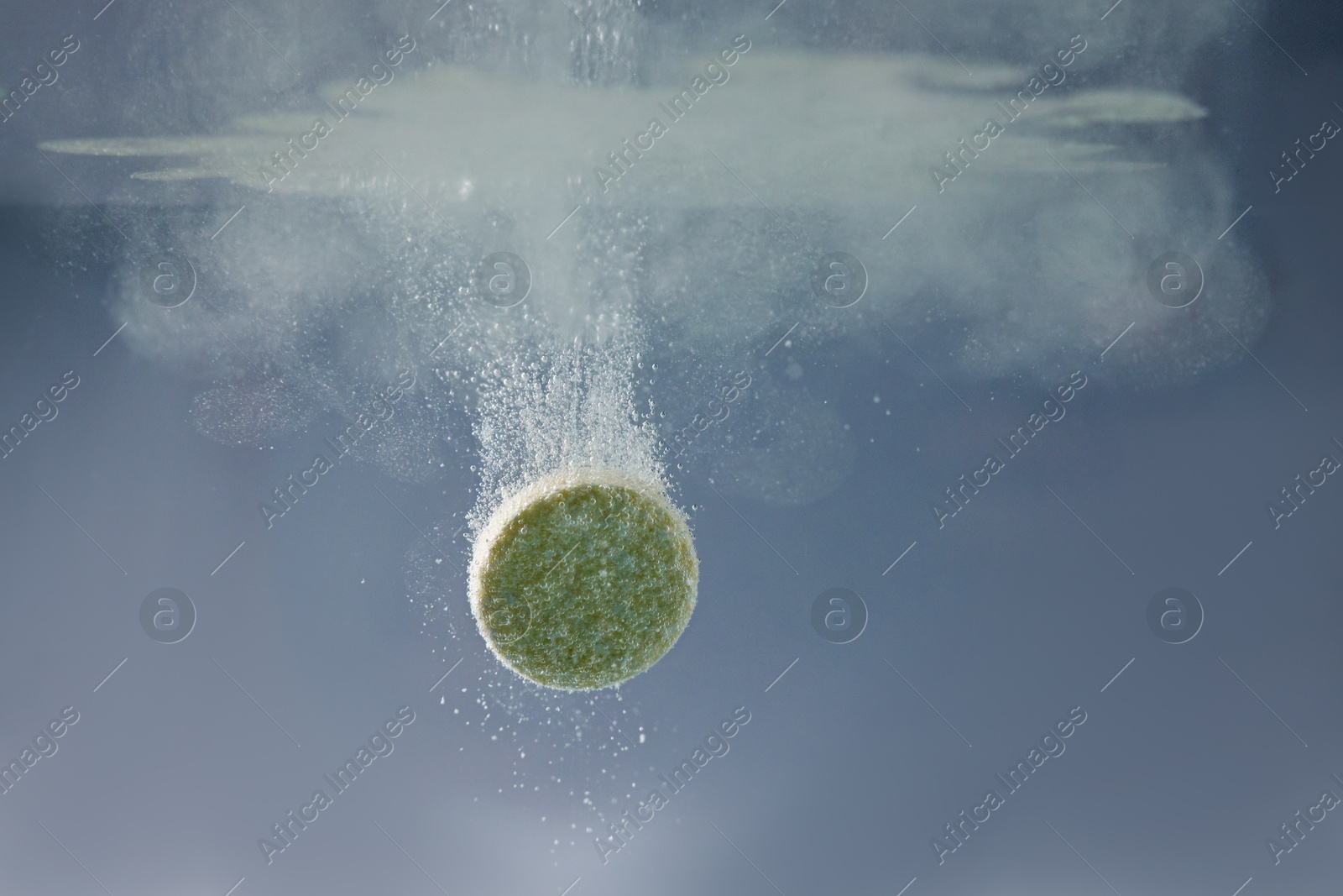 Photo of Effervescent pill dissolving in water on grey background, closeup