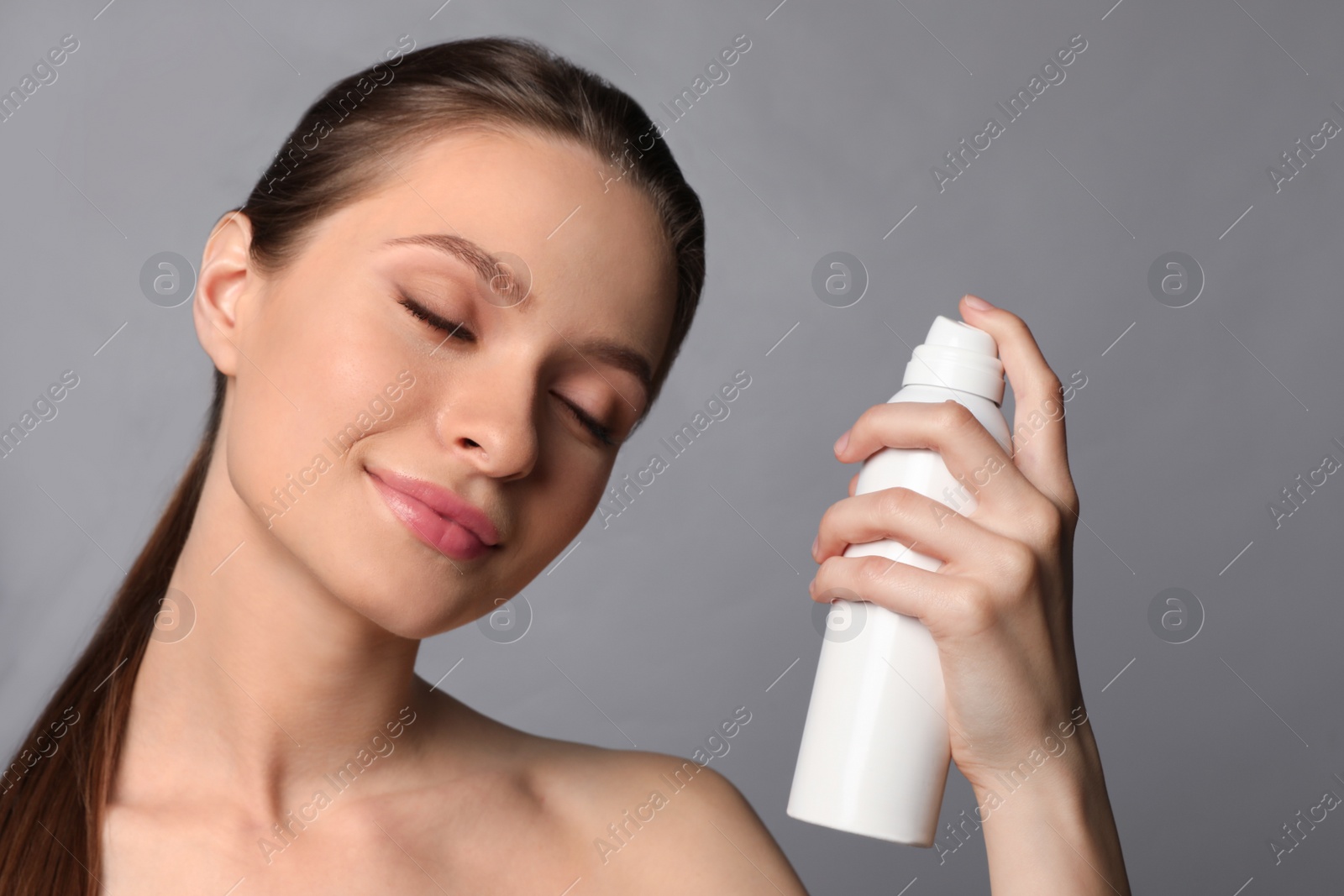 Photo of Young woman applying thermal water on face against grey background. Cosmetic product