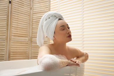 Beautiful woman taking bath with foam in tub indoors