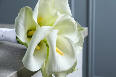 Photo of Beautiful calla lily flowers tied with ribbon on grey table, closeup