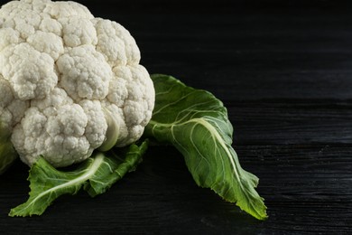 Fresh whole cauliflower on black wooden table, closeup. Space for text