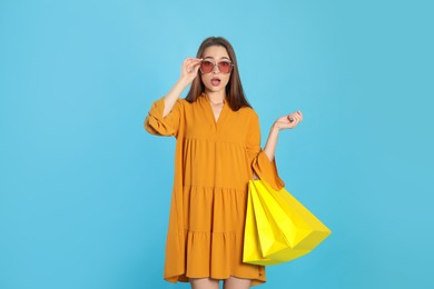 Photo of Surprised young woman with shopping bags on light blue background. Big sale