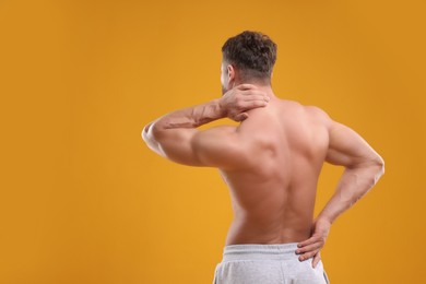 Photo of Man suffering from back and neck pain on orange background, back view. Space for text