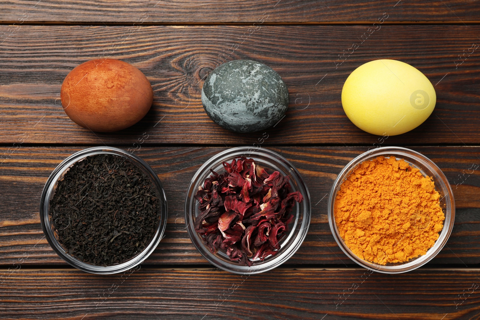 Photo of Painted Easter eggs with natural organic dyes (hibiscus, turmeric and tea) on wooden table, flat lay