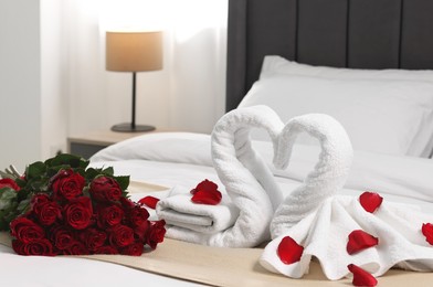 Photo of Honeymoon. Swans made of towels and beautiful red roses on bed in room