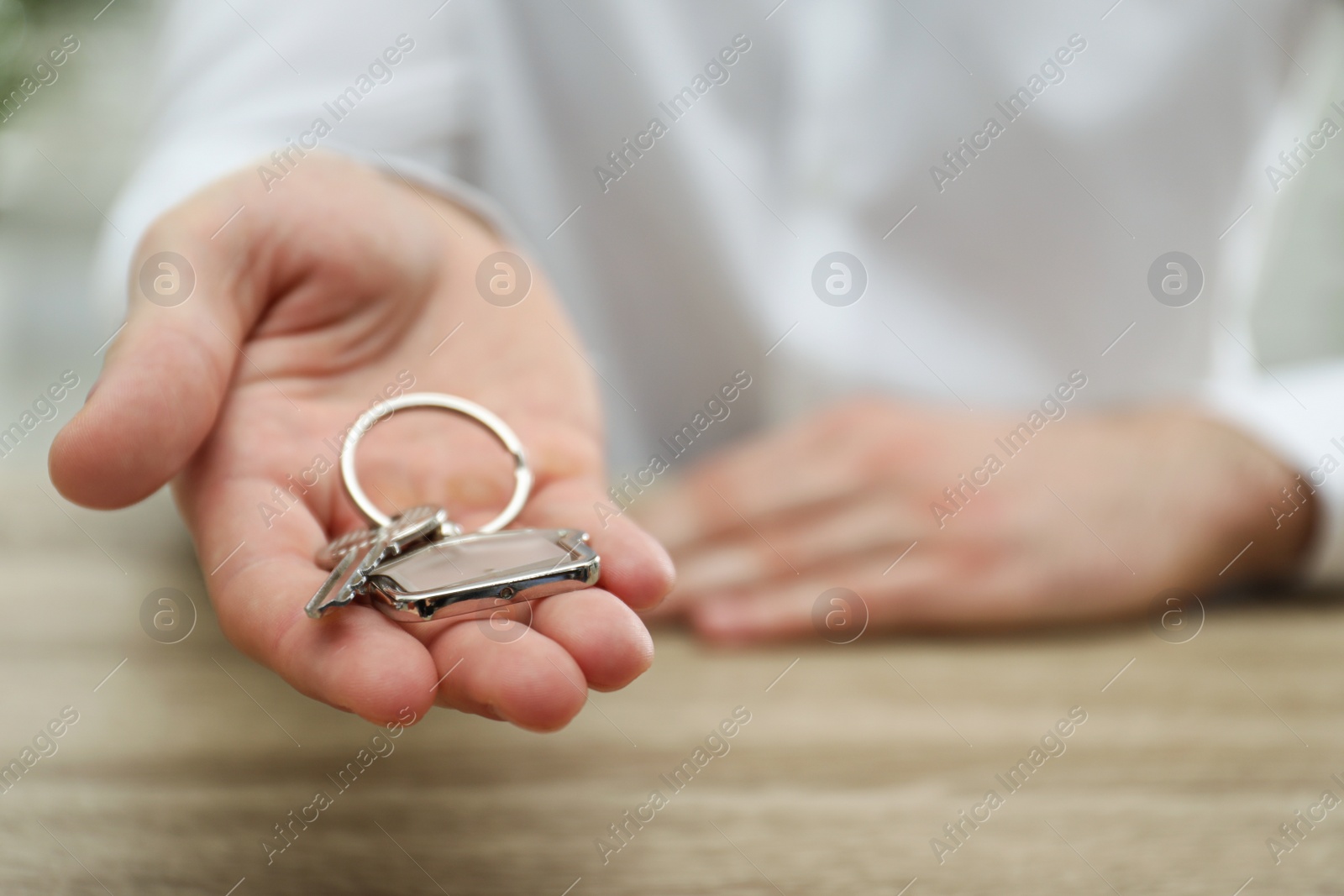 Photo of Real estate agent holding house key with trinket at wooden table, closeup