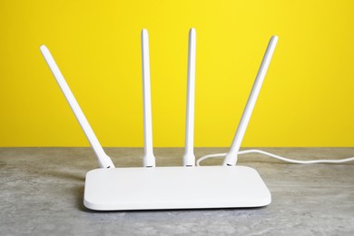 Photo of New white Wi-Fi router on grey textured table against yellow background