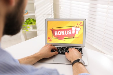 Image of Bonus gaining. Man using laptop at white table indoors, closeup. Illustration of gift box and word on device screen