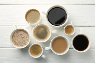 Different coffee drinks in cups on white wooden table, flat lay