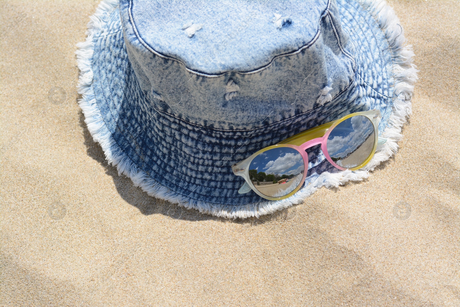 Photo of Jeans hat and sunglasses on sand, above view. Beach accessories