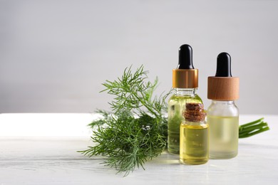 Photo of Bottles of essential oil and fresh dill on white wooden table, space for text