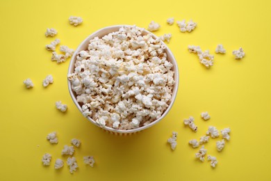 Photo of Paper bucket with delicious popcorn on yellow background, flat lay