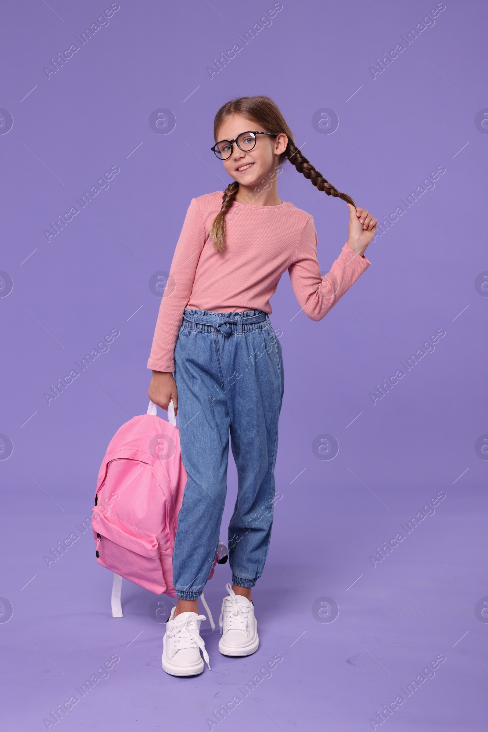 Photo of Happy schoolgirl with backpack on violet background