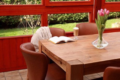 Photo of Glass of delicious cocoa, pink tulips and book on wooden table at terrace